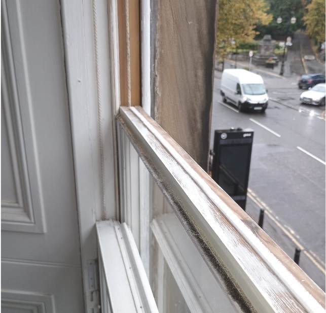 Close-up of a timber sash window showing brush draught-proofing seals along the sash edge